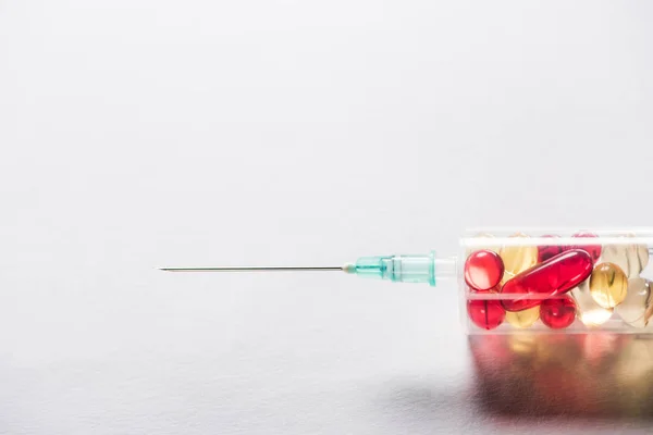 Close up of syringe with red and yellow pills on grey background — Stock Photo