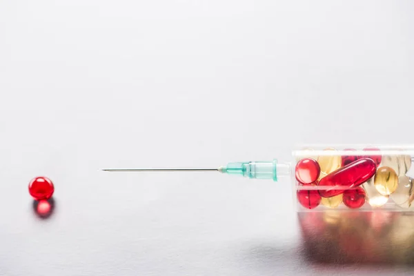 Fechar a seringa com medicação perto da pílula redonda vermelha no fundo cinzento — Fotografia de Stock