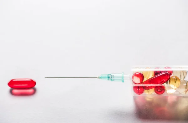 Крупним планом шприц з ліками біля червоної овальної таблетки на сірому фоні — стокове фото