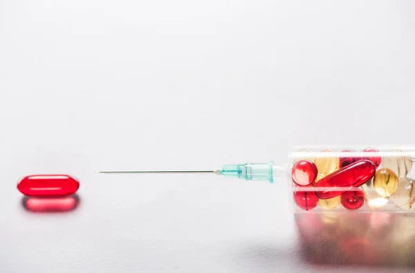 Primer plano de la jeringa con medicamentos cerca de la píldora ovalada roja sobre fondo gris - foto de stock