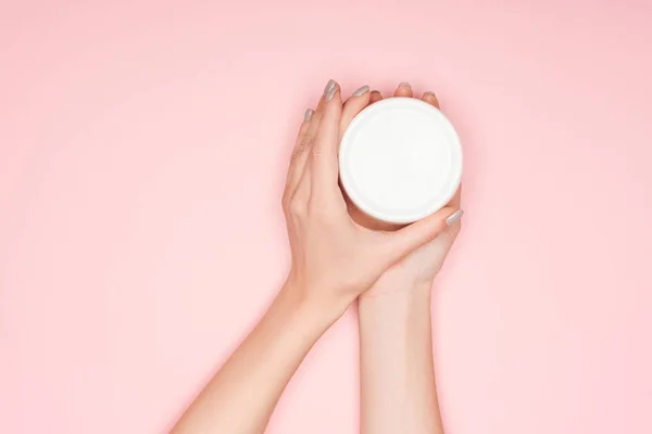 Vista parcial de las manos femeninas con crema corporal aislada en rosa - foto de stock
