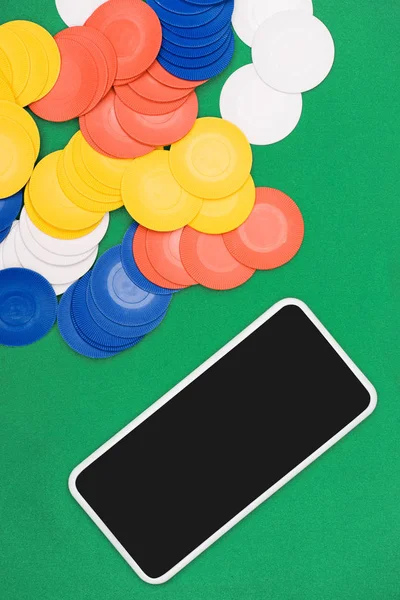 Vista superior de la mesa de póquer verde con fichas multicolores y teléfono inteligente - foto de stock
