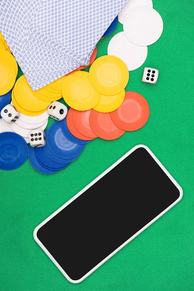 Vista superior de la mesa de póquer verde con fichas multicolores, naipes, dados y smartphone - foto de stock