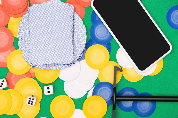 Vista dall'alto del tavolo da poker verde con chip multicolori, carte da gioco, dadi, bastone e smartphone — Foto stock