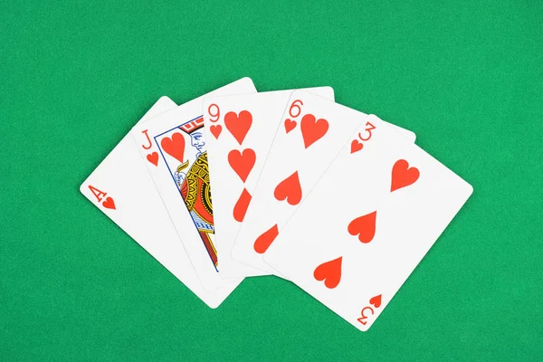 Top view of green poker table and unfolded playing cards with hearts suit — Stock Photo