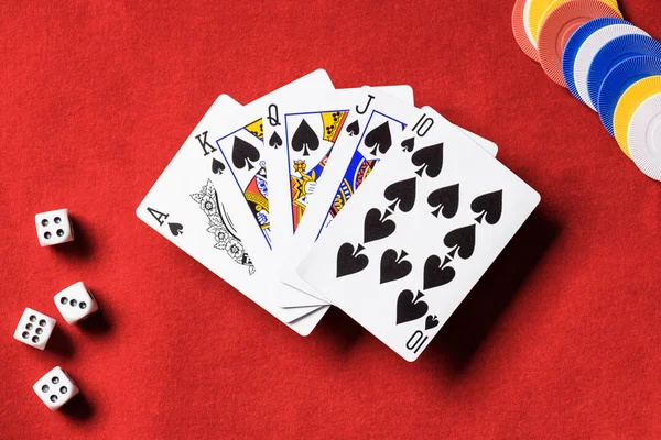 Top view of red poker table and multicolored chips, dices, unfolded playing cards with spades suit — Stock Photo