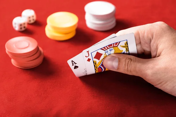 Messa a fuoco selettiva di uomo in possesso di carte da gioco con fiches e dadi su sfondo — Foto stock