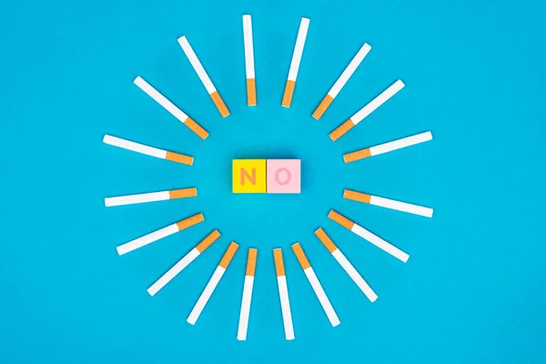 Couché plat avec des cubes de lettres colorées et des cigarettes isolées sur bleu, arrêter de fumer concept — Photo de stock