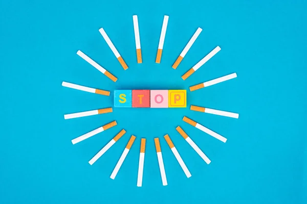 Flat lay with cigarettes and colorful letter blocks isolated on blue, stop smoking concept — Stock Photo