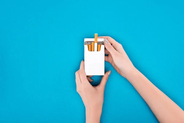 Partial shot of woman holding pack of cigarettes isolated on blue — Stock Photo