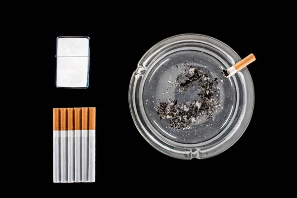 Flache Lage aus Glasaschenbecher, Feuerzeug und Zigaretten isoliert auf schwarz — Stockfoto