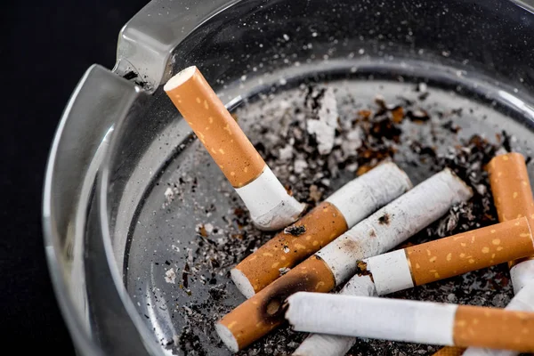 Close up shot of cigarette butts in glass ashtray — Stock Photo