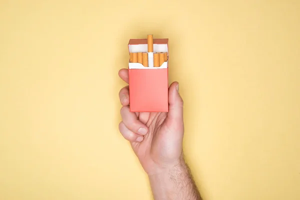 Vista recortada del hombre sosteniendo paquete rojo de cigarrillos aislados en amarillo - foto de stock