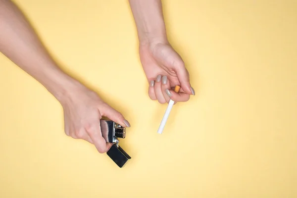 Partial view of woman holding cigarette and cigarette lighter isolated on yellow — Stock Photo