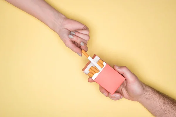 Partial view of man treats woman with cigarette isolated on yellow — Stock Photo