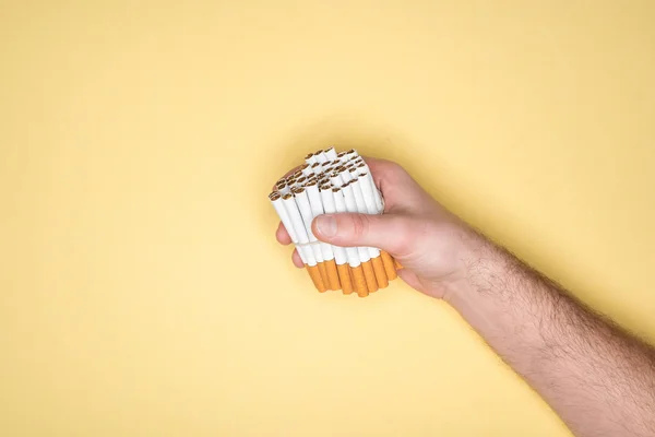 Vista parcial del hombre sosteniendo cigarrillos en puño aislado en amarillo - foto de stock