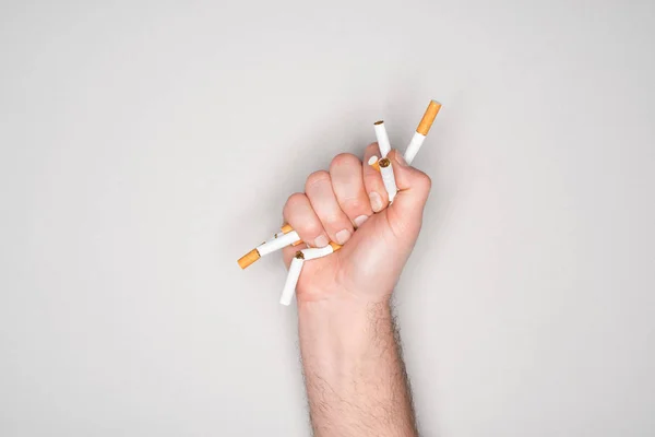 Vue partielle de l'homme brisant des cigarettes à la main isolé sur gris, arrêter de fumer concept — Photo de stock