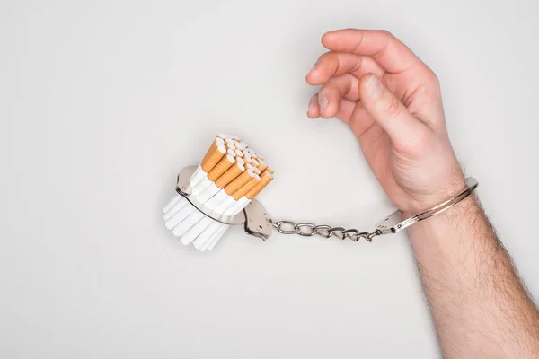 Teilbild eines Mannes in Handschellen, der mit Zigaretten isoliert auf grauem, Nikotinabhängigkeitskonzept posiert — Stockfoto