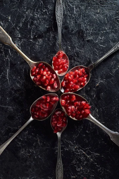 Flat lay with garnet seeds and spoons on black surface — Stock Photo