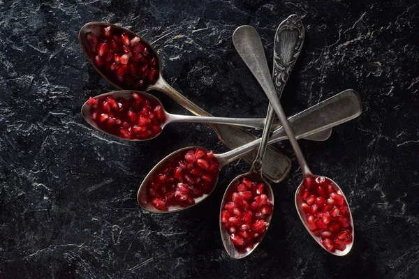 Flat lay of silverware and pomegranate seeds on dark background — Stock Photo