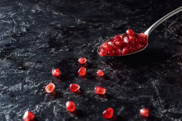 Studio shot of spoon and garnet seeds on black surface — Stock Photo