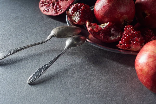 Studio shot of spoons and ripe garnets on plate — Stock Photo