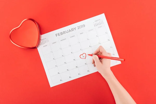 Vista recortada de la mujer que marca con corazón 14 de febrero fecha en el calendario aislado en rojo, San Valentín concepto de día - foto de stock