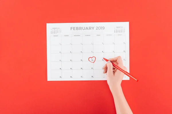 Vista cortada da mulher segurando marcador sobre o calendário com data de 14 de fevereiro marcado isolado no vermelho, st dia dos namorados conceito — Fotografia de Stock