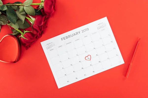 Vue du haut des roses et calendrier avec 14 février date marquée avec coeur isolé sur rouge, concept St Valentin — Photo de stock