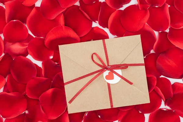 Vue du haut de l'enveloppe avec ruban et pétales de rose rouge sur le fond, concept St Valentin — Photo de stock