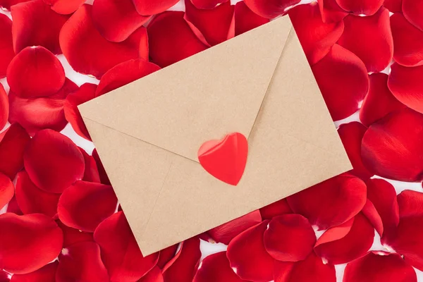 Верхний вид конверта с сердцем и красными лепестками роз на заднем плане, День святого Валентина — стоковое фото
