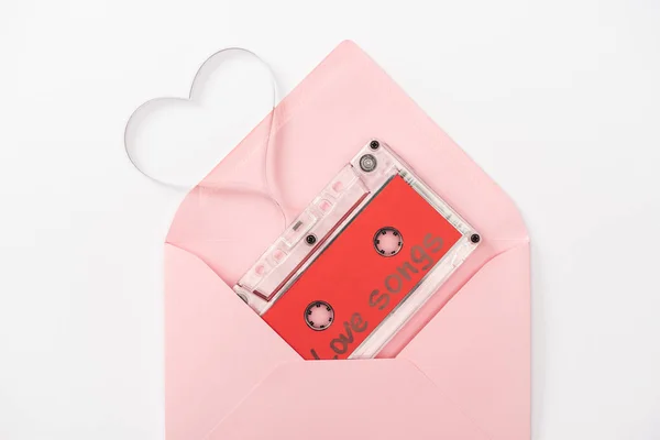 Vista superior del casete de audio con letras de 'canciones de amor' y símbolo del corazón en sobre aislado en blanco, concepto de San Valentín - foto de stock