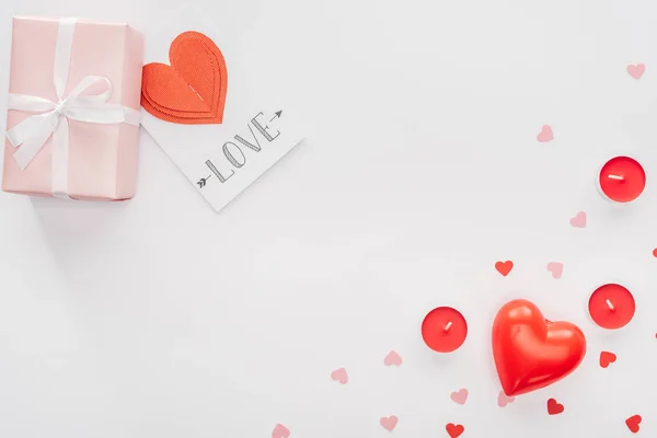 Vista superior de la caja de regalo, corazones de papel y tarjeta de felicitación con letras de 'amor' aisladas en blanco, San Valentín concepto de día - foto de stock