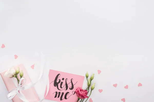 Vista superior de flores, caja de regalo y tarjeta con letras 'kiss me' aisladas en blanco - foto de stock