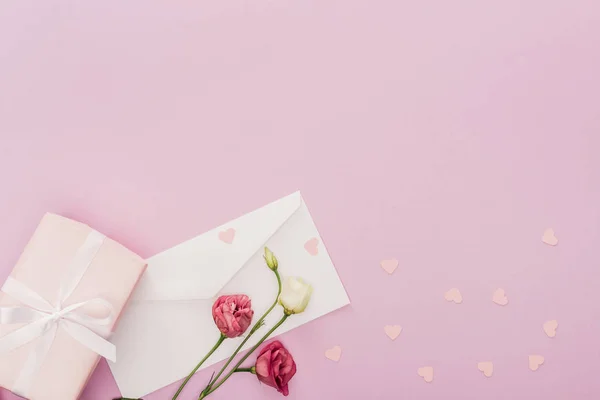Vista superior del sobre, caja de regalo, flores y corazones de papel aislados en rosa - foto de stock