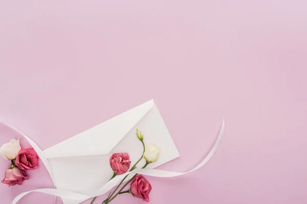 Vista superior de flores, fita e envelope isolado em rosa com espaço de cópia — Fotografia de Stock