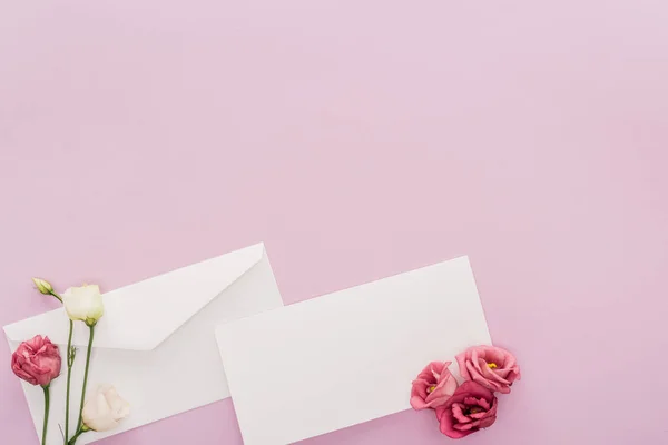 Vista superior de la tarjeta en blanco, sobre y flores aisladas en rosa con espacio para copias - foto de stock