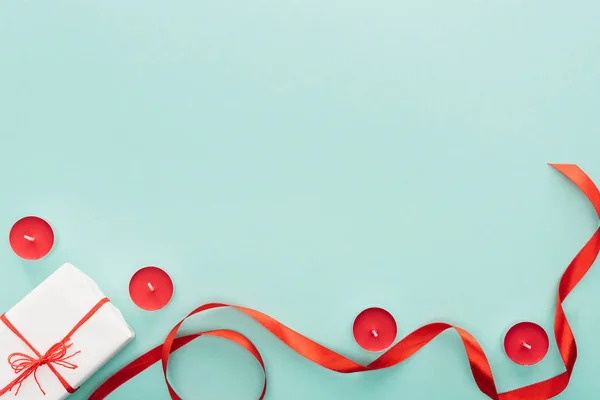 Vista superior de cinta roja, caja de regalo y velas aisladas en turquesa - foto de stock