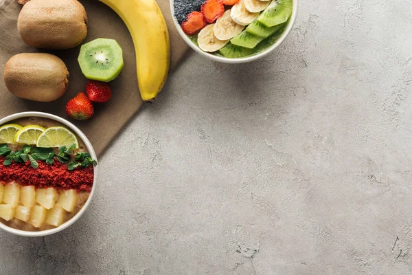 Vista superior de tigelas de smoothie com frutas frescas e ingredientes orgânicos em fundo cinza com espaço de cópia — Fotografia de Stock