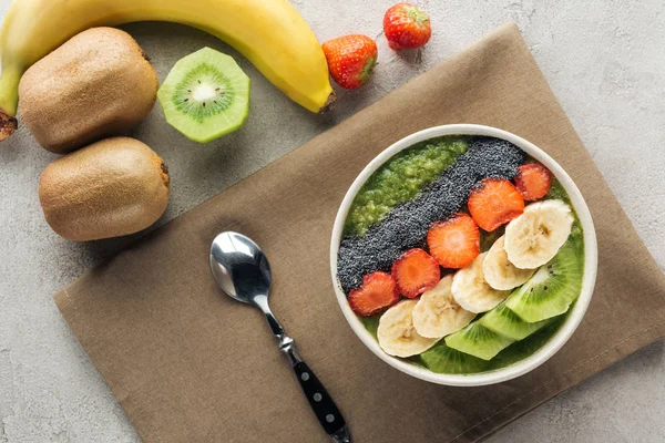 Vista superior del tazón de batido con frutas frescas, cuchara e ingredientes sobre fondo gris - foto de stock