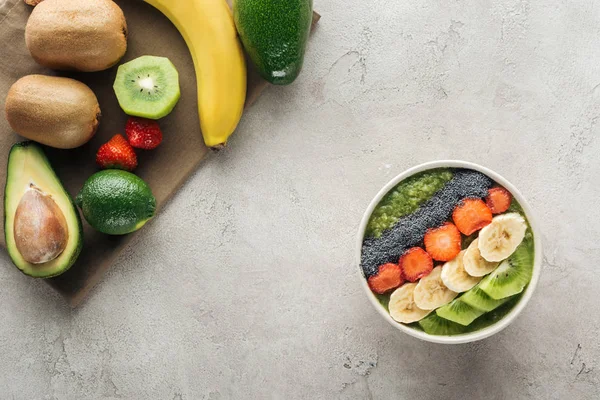 Top view of smoothie bowl with fresh fruits and ingredients on grey background with copy space — Stock Photo
