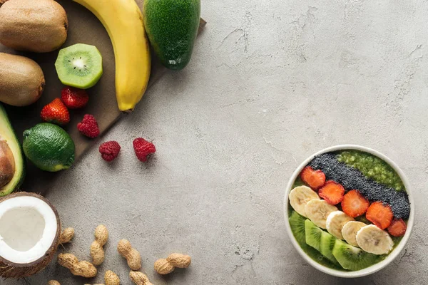 Vista superior del tazón de batido con frutas frescas y frutos secos sobre fondo gris - foto de stock