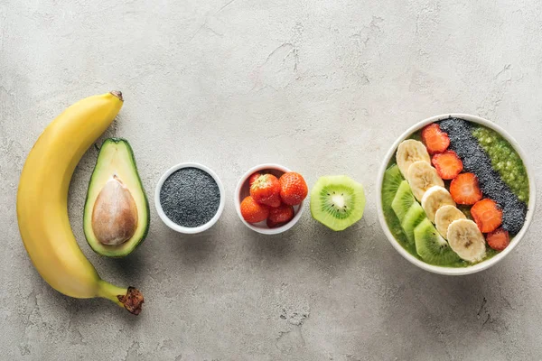 Вид зверху здорової миски з свіжими фруктами та інгредієнтами на сірому фоні — стокове фото