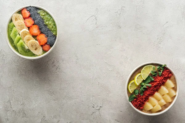 Vue du dessus des bols de smoothie bio sain avec des fruits sur fond gris avec espace de copie — Photo de stock