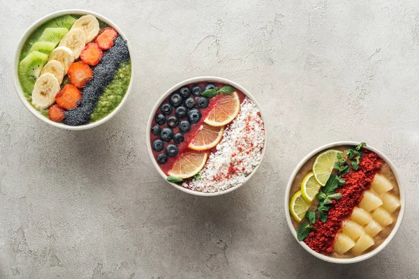 Top view of healthy organic smoothie bowls with fruits on grey background — Stock Photo