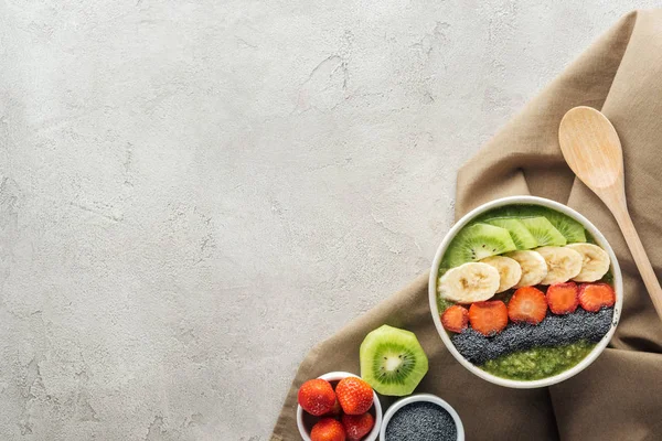 Top view of smoothie bowl, wooden spoon and ingredients on grey background with copy space — Stock Photo