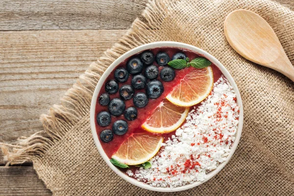 Top view of healthy organic smoothie bowl with blueberries, lemons and shredded coconut on sackcloth — Stock Photo