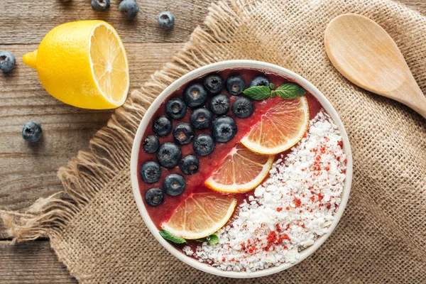 Top view of healthy organic smoothie bowl with blueberries, lemons and shredded coconut on sackcloth — Stock Photo