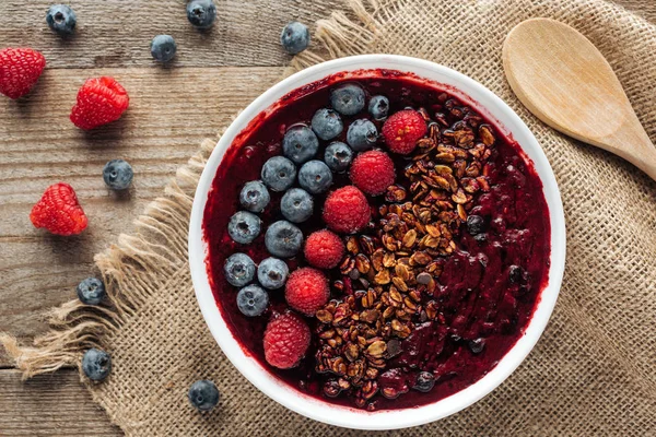 Vista superior del tazón de batido orgánico fresco con bayas y granola en tela de saco - foto de stock