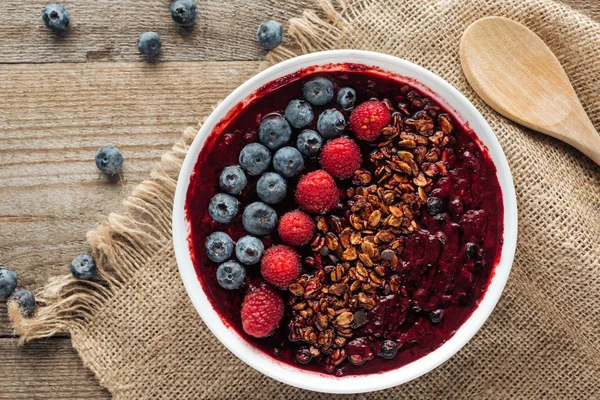 Vista superior del tazón de batido orgánico fresco con bayas y granola en tela de saco - foto de stock